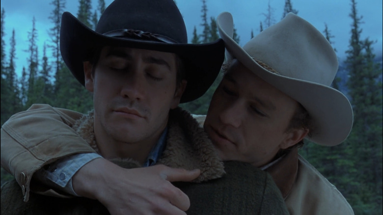 Heath Ledger as Ennis Del Mar and Jake Gyllenhaal as Jack Twist in Brokeback Mountain, with Ennis embracing Jack from behind out in the trees.