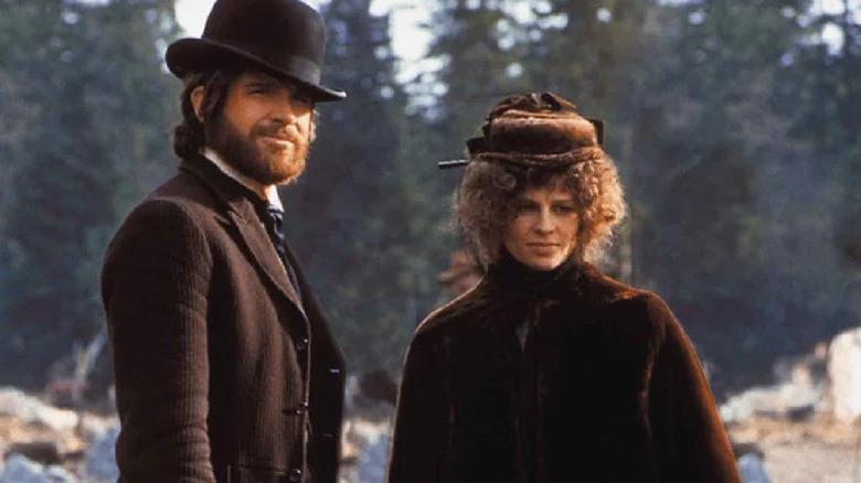John McCabe (Warren Beatty) and Constance Miller (Julie Christie) stand next to each other by a forest in McCabe & Mrs. Miller