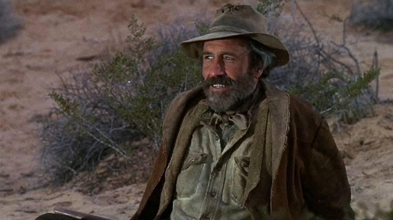 Cable Hogue (Jason Robards) grins while sitting on the ground in The Ballad of Cable Hogue