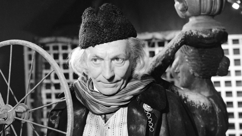 The First Doctor (William Hartnell) stands near a wheel contraption in Doctor Who