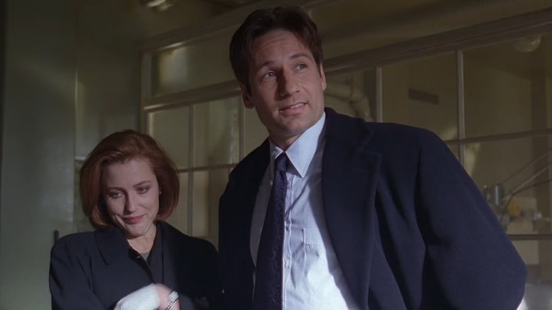 Dana Scully (Gillian Anderson) smirks skeptically as Fox Mulder (David Duchovny) smiles smugly in The X-Files (1993)
