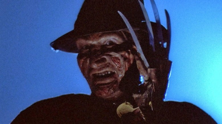 Robert Englund as Freddy Krueger smiling and holding up his hand with his knife glove on it in A Nightmare on Elm Street