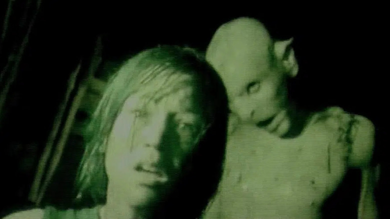 Alex Reid as Beth looking scared with a deformed humanoid creature standing behind her in night vision in The Descent