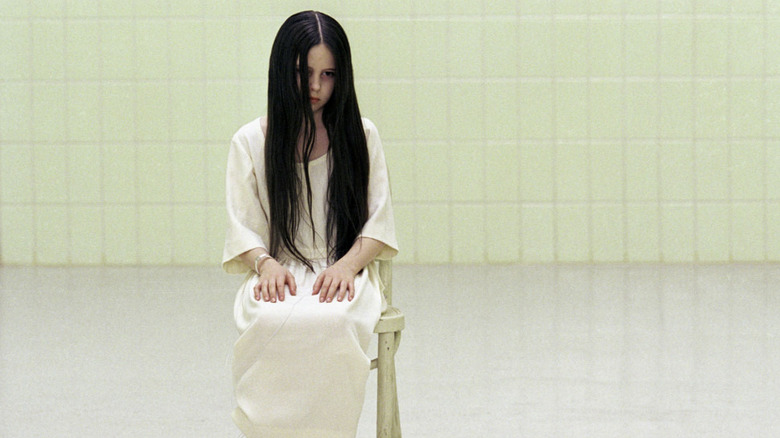 Daveigh Chase as Samara sitting on a chair in a white room wearing a white dress in The Ring