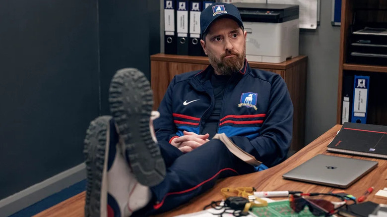 Coach Beard (Brendan Hunt) with shoes on desk on Ted Lasso