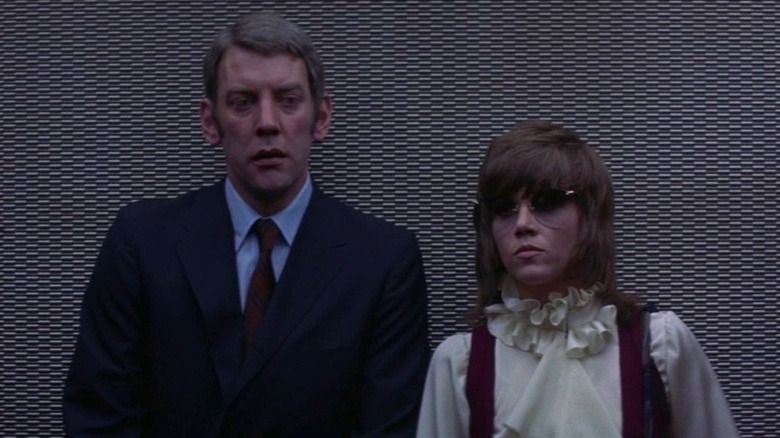 Donald Sutherland as Detective John Klute in suit standing next to Jane Fonda as Bree in white blouse and sunglasses in Klute