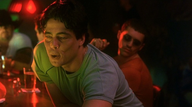 Benicio del Toro as Javier Rodríguez Rodríguez leaning forward in red-lit bar in Traffic