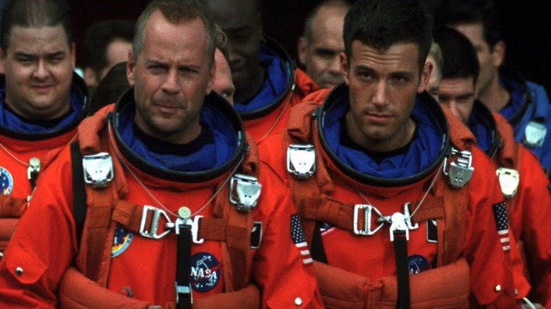 Harry Stamper (Bruce Willis) and AJ walk towards a space shuttle with their crew in spacesuits in Armageddon (1998)