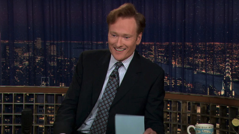 Conan O'Brien laughs at his desk on Late Night With Conan O'Brien