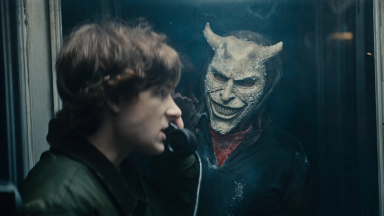 Finney talks on a payphone with the Grabber watches in Black Phone 2