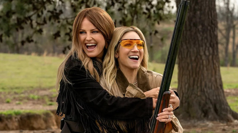 Malin Akerman and Brittany Snow as Margo and Sophie, laughing and embracing wild hunting in the woods in The Hunting Wives