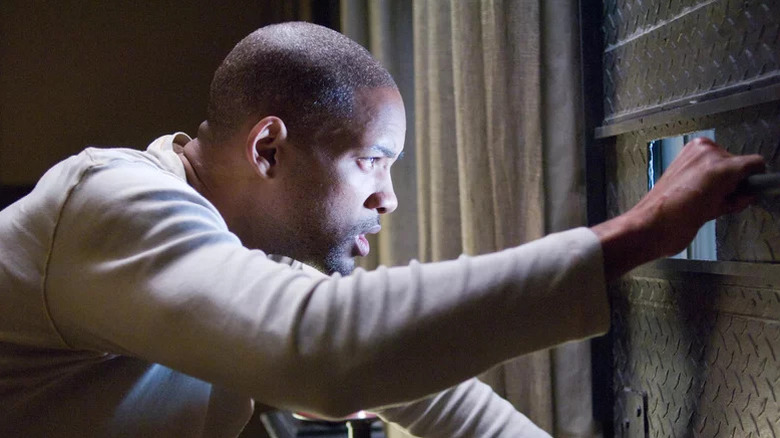 Dr. Robert Neville (Will Smith) peering through a door in I Am Legend