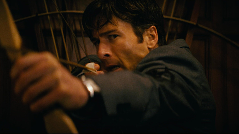 Glen Powell as Becket Redfellow in How To Make A Killing, wielding a bow and arrow and about to fire.