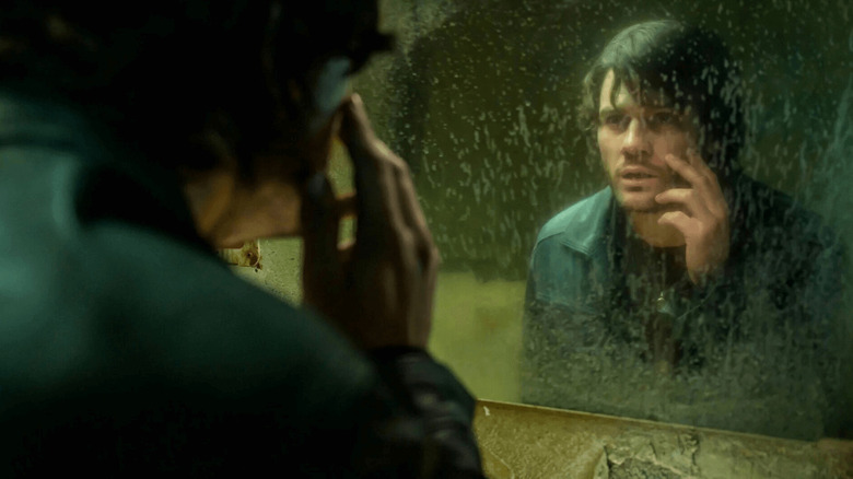 Jeremy Irvine as James Sunderland in Return to Silent Hill, touching his face as he looks in a dirty mirror.