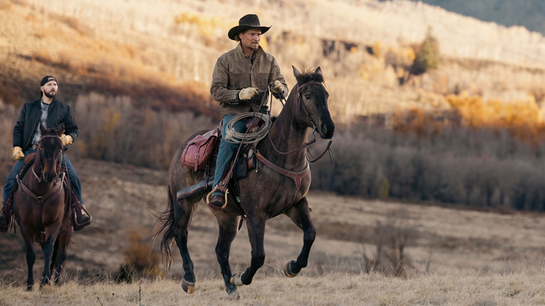 Luke Grimes as Kayce Dutton in Marshals, riding a horse with Logan Marshall-Green as Pete Calvin riding behind him.