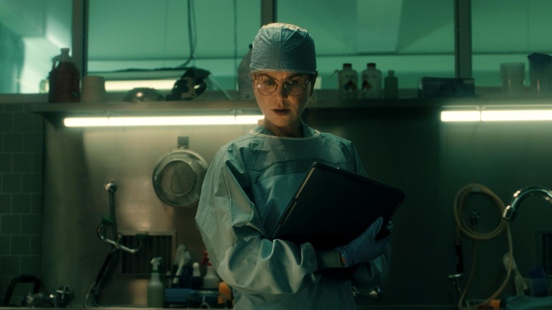 Nicole Kidman as Kay Scarpetta in Scarpetta, in her surgeon scrubs, holding a device in her hands as she looks down.