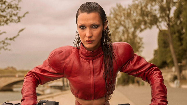 Bella Hadid as Ruby in The Beauty, wearing a cropped red leather jacket on a motorbike.