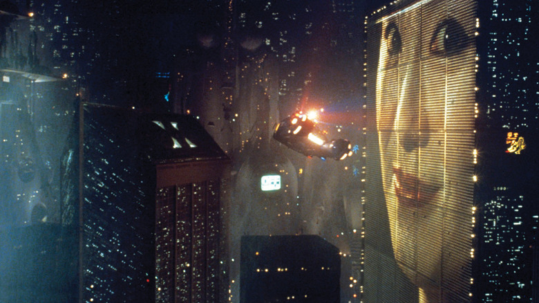 A flying car cruises through skyscrapers at night in Blade Runner