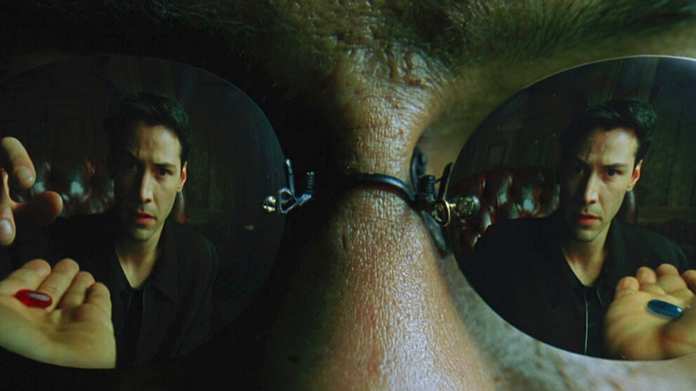 Neo (Keanu Reeves) looks at the red pill and blue pill in the reflection of Morpheus' sunglasses in The Matrix