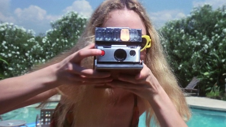 Heather Graham as Rollergirl in Boogie Nights, holding up a camera directly to the view of the audience in front of a swimming pool.