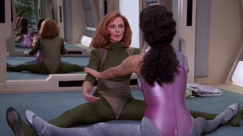Beverly Crusher (Gates McFadden) and Deanna Troi (Marina Sirtis) stretch together on the floor in Star Trek: The Next Generation