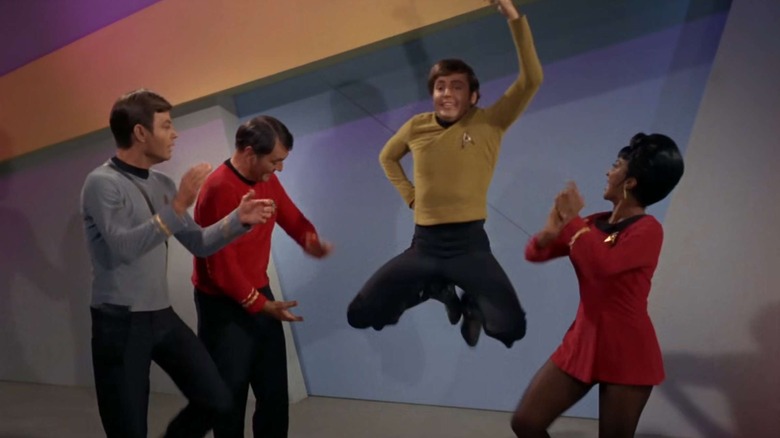 Pavel Chekhov (Walter Koenig) leaps in a Russian dance as his crew mates applaud in Star Trek: The Original Series