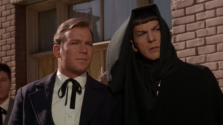 Kirk (William Shatner) and Spock (Leonard Nimoy) wear 19th century disguises by a brick wall in Star Trek: The Original Series