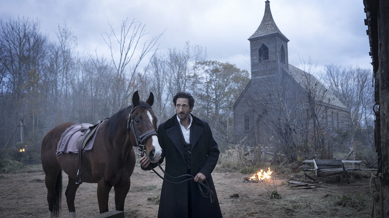Charles Boone (Adrien Brody) leads a horse by a church in Chapelwaite