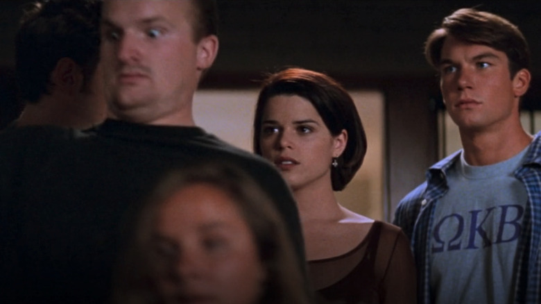 Randy Meeks (Jamie Kennedy) speaks with Sydney Prescott (Neve Campbell) and Derek Feldman (Jerry O'Connell) in Scream 2 while an extra acts poorly in front of them