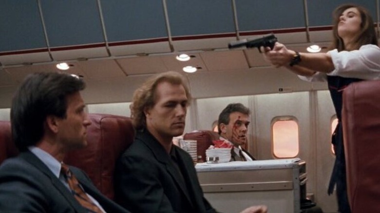 Sabrina Ritchie (Elizabeth Hurley) aims a gun over Charles Rane (Bruce Payne) with a bloody passenger in the background in Passenger 57
