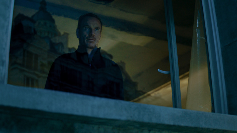 The killer (Michael Fassbender) stares outside of a window in The Killer (2023)