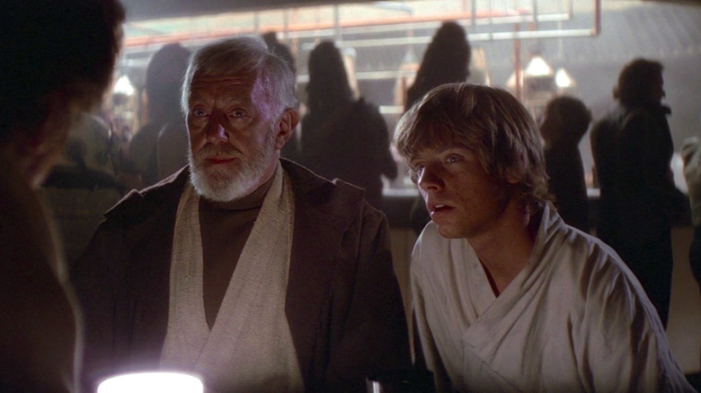 Mark Hamill as Luke Skywalker and Alec Guinness as Obi-Wan "Ben" Kenobi in Star Wars: Episode IV - A New Hope, sitting next to each other at the cantina and looking across the table.