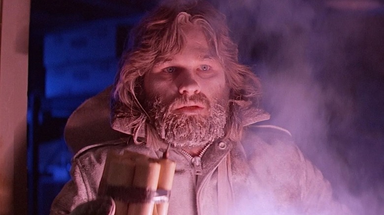 Kurt Russell as R. J. MacReady in The Thing, looking frostbitten and illuminated by a light source beneath him, seemingly holding explosives.
