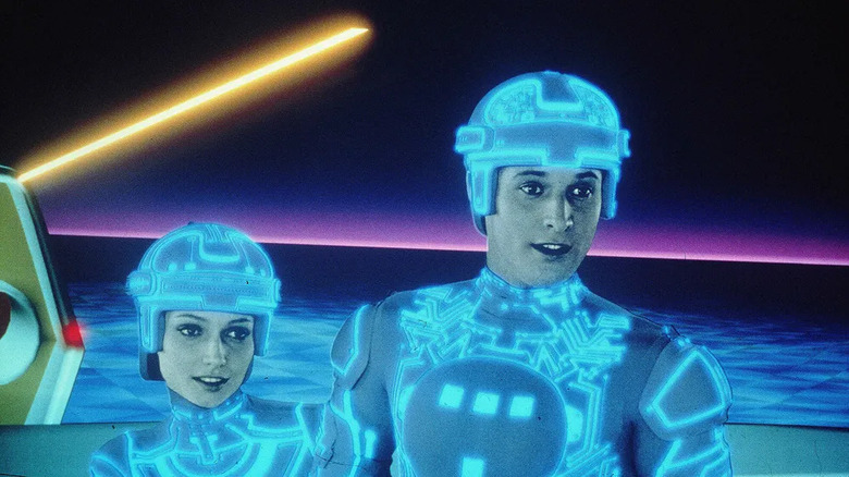 Cindy Morgan as Lora Baines/Yori and Bruce Boxleitner as Alan Bradley/Tron in Tron, standing in the neon-lit digital grid together.