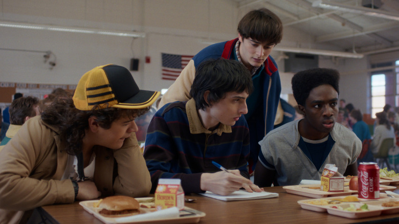 Dustin (Gaten Matarazzo), Mike (Finn Wolfhard), Will (Noah Schnapp), and Lucas (Caleb McLaughlin) sitting at a table at lunch on Stranger Things