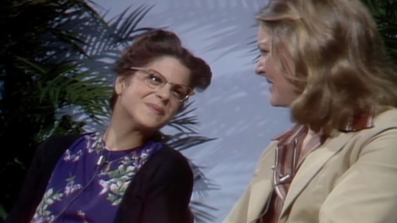 Gilda Radner as Emily Litella smiling at Jane Curtin in a Looks on Books sketch on SNL
