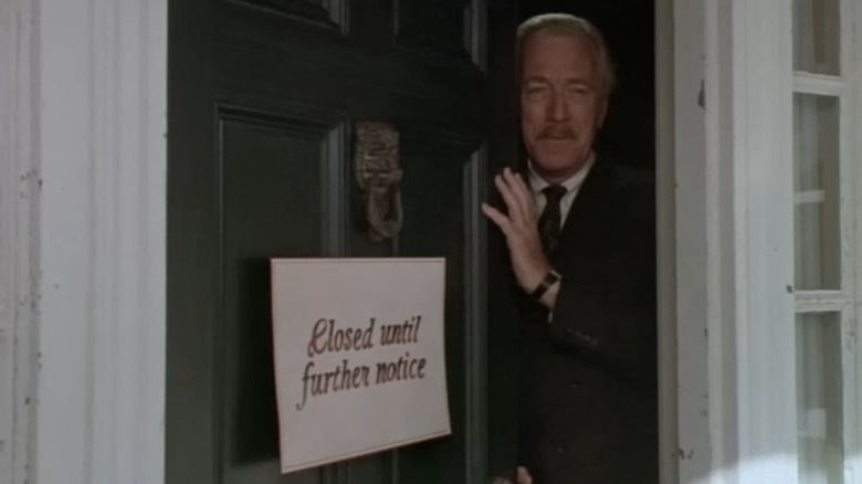 Max Von Sydow as Leland Gaunt in Needful Things, peering out of the shop door, which has a "closed until further notice" sign on it