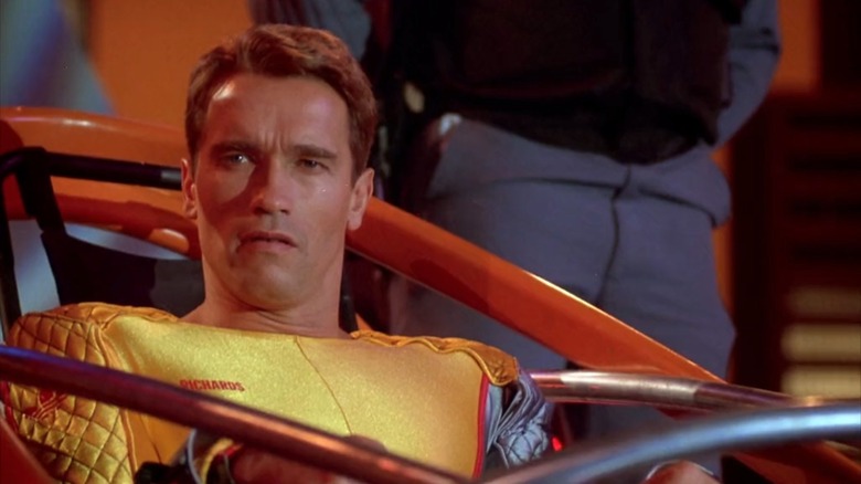 Arnold Schwarzenegger as Richards in The Running Man, wearing a gold suit and strapped into a sled