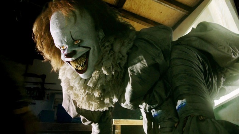 Pennywise (Bill Skarsgård) crawls out of a projection, bigger and with sharpened fangs, in It