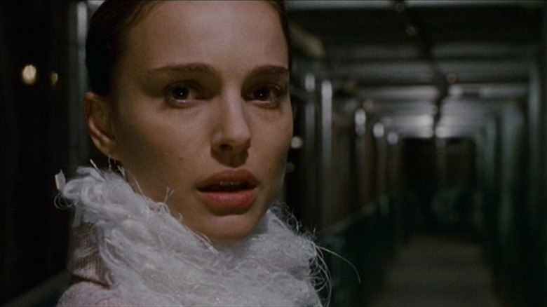 Natalie Portman as Nina in Black Swan, looking afraid in a hallway, a white feathery scarf around her neck