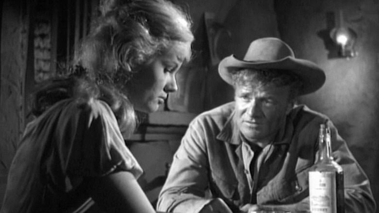 Addie McKeen (Marie Selland) looks down as Dave Blassingame (Brian Keith) talks to her over a bottle of whiskey in The Westerner