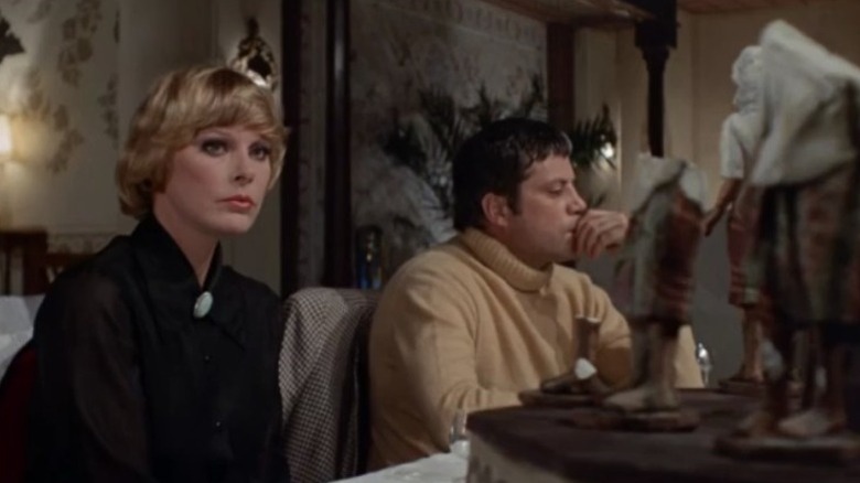 Elke Sommer as Vera Clyde and Oliver Reed as Hugh Lombard sitting at a table and looking at the figurines in And Then There Were None