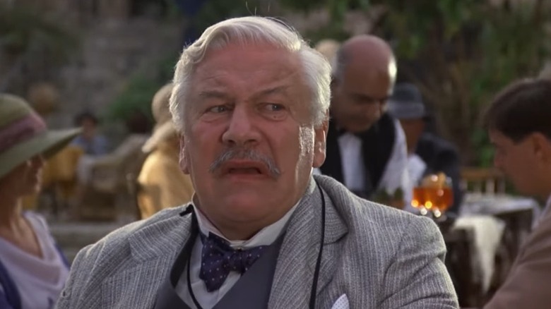 Peter Ustinov as Hercule Poirot looking uncomfortably to his left while sitting at an outdoor table in Appointment with Death
