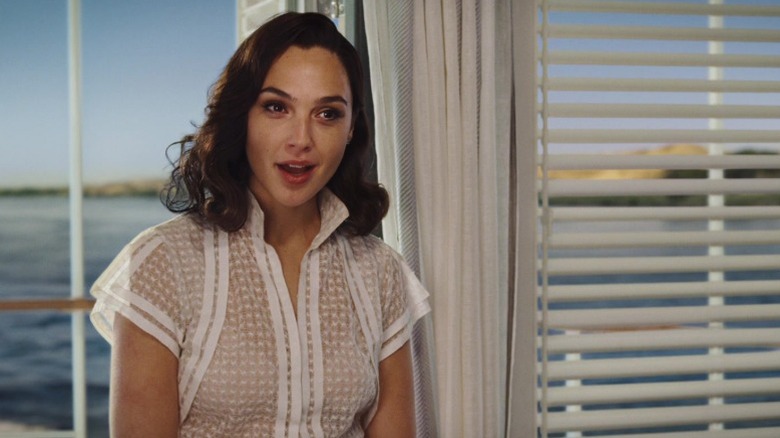 Gal Gadot as Linnet Ridgeway standing in front of a balcony door and speaking in Death on the Nile