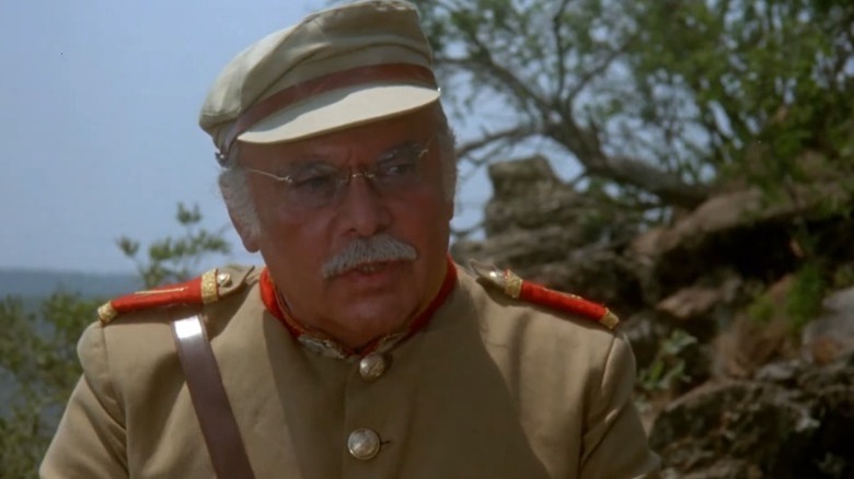 Herbert Lom as General Romensky standing in front of rocks and trees in Ten Little Indians