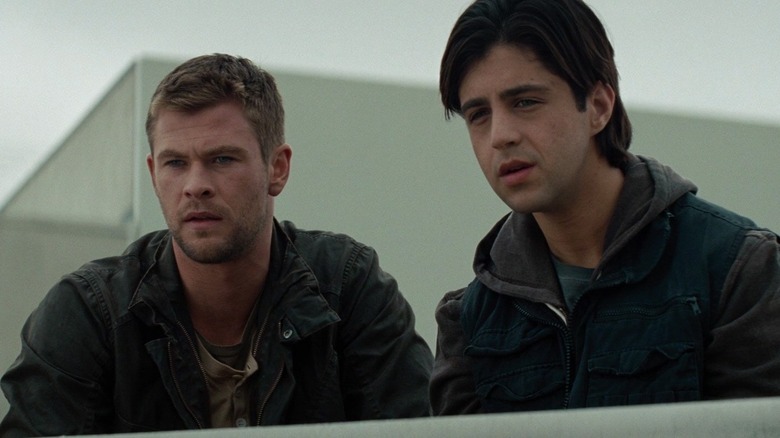 Chris Hemsworth as Jed Eckert and Josh Peck as Matt Eckert in Red Dawn, standing next to each other as they look off at something.