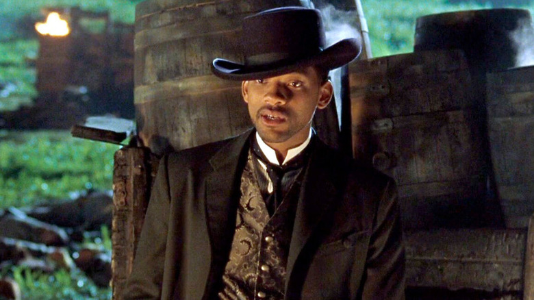 Will Smith as U.S. Army Captain James T. "Jim" West in Wild Wild West, wearing a vest, suit jacket, and brimmed black hat in front of a cart of barrels.