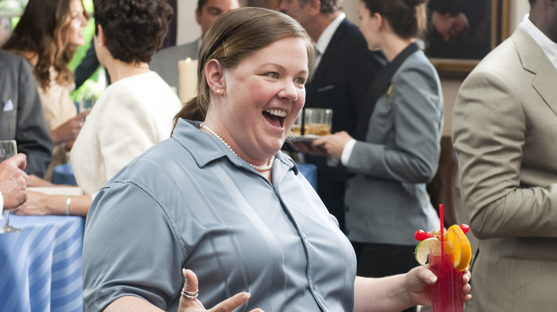 Megan holding a drink and cheering in Bridesmaids