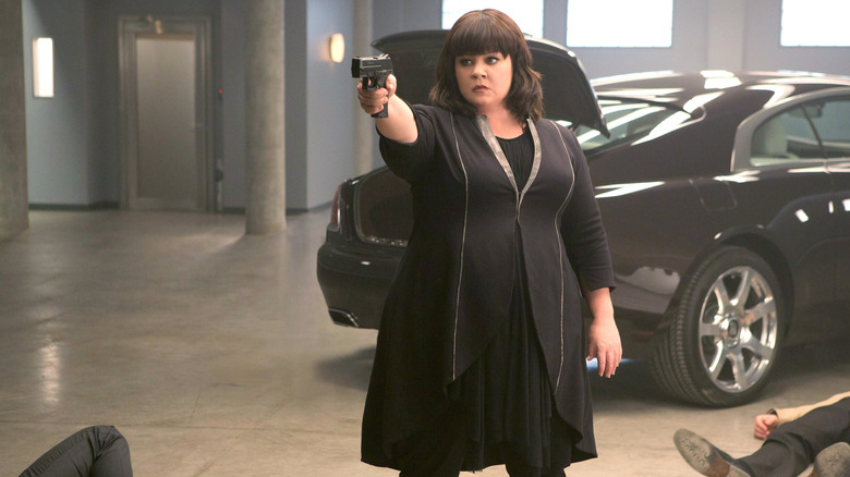 Susan in a sleek black outfit pointing a gun at someone offscreen in Spy