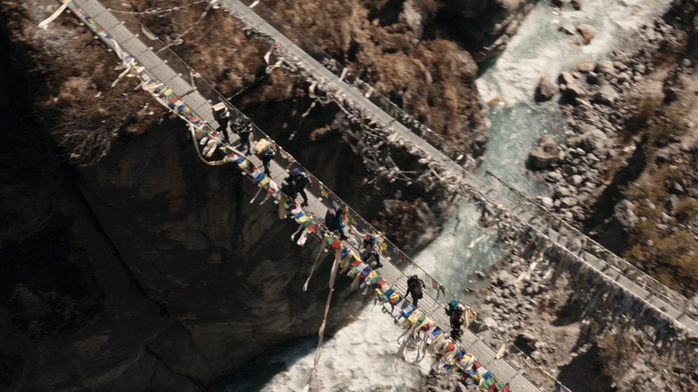 A top down view shows an expedition crossing a bridge over a river in Everest